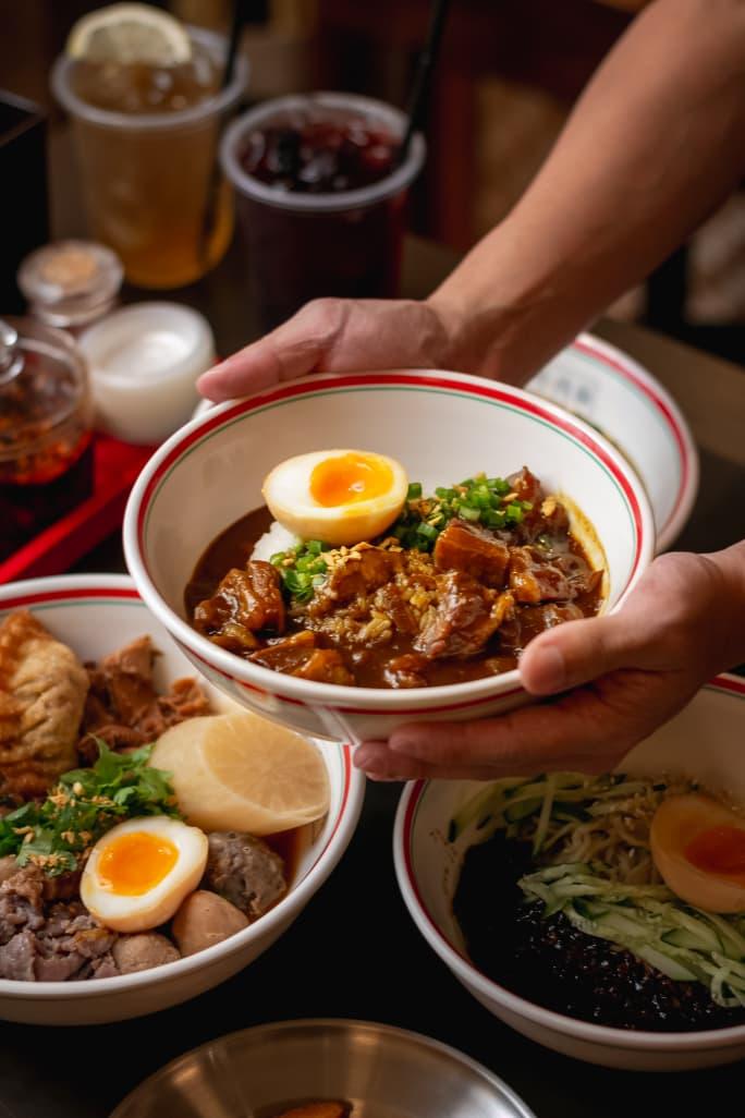 Braised beef rice bowl held with two hands — Teowkee branded bowl with soft-boiled egg