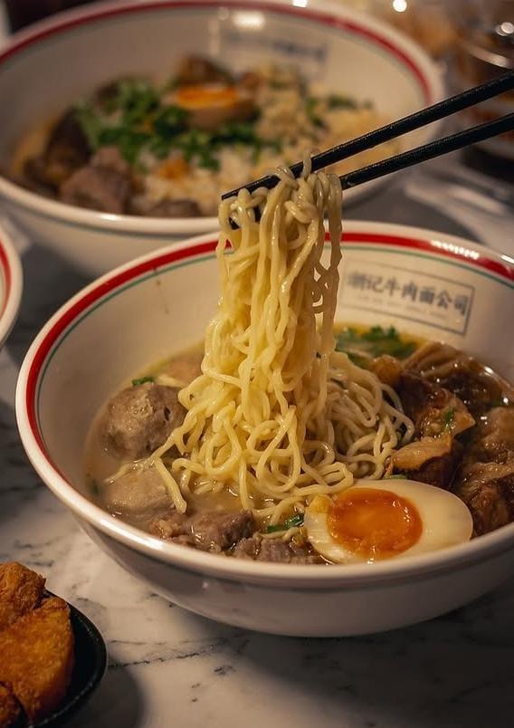 Chopsticks lifting noodles from a Teowkee beef noodle soup bowl