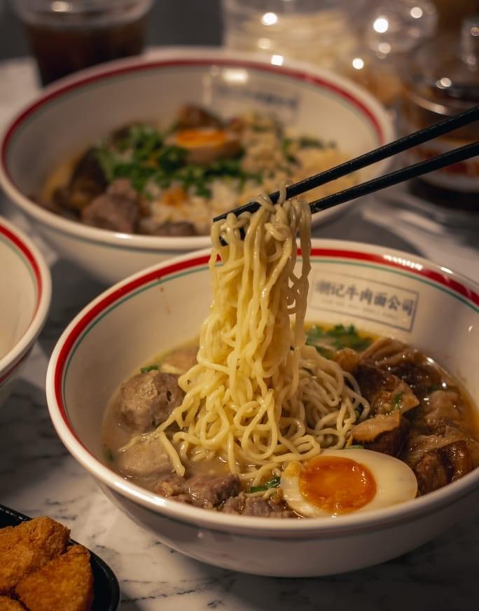 Teowkee beef noodle soup — chopsticks lifting golden noodles from branded bowl