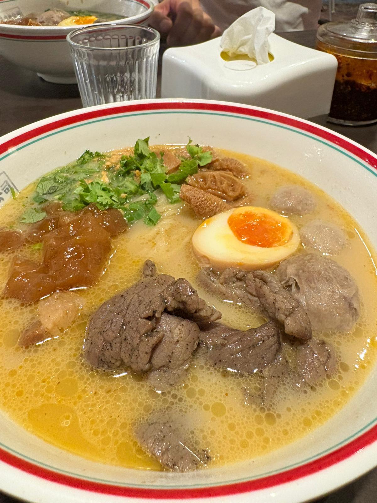 Teowkee beef noodle soup close-up — clear broth, beef slices, tendon, soft-boiled egg