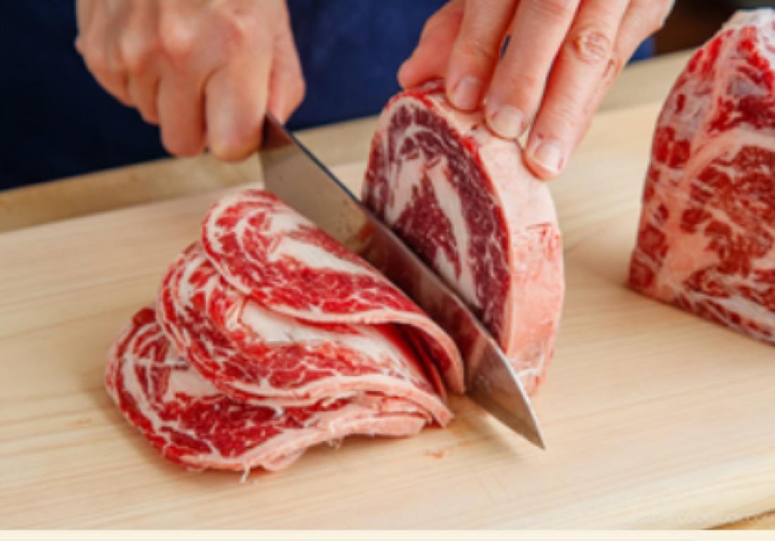 Hands slicing fresh marbled beef on a wooden board